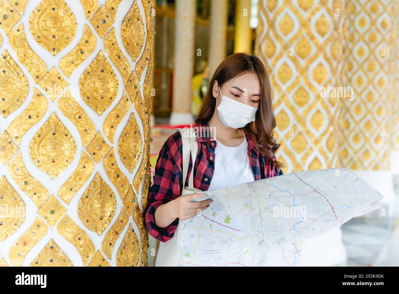 Portrait jeune femme de routard asiatique dans le masque debout et tenir la carte de papier à la main au beau temple thaïlandais, elle cherche la direction Banque D'Images