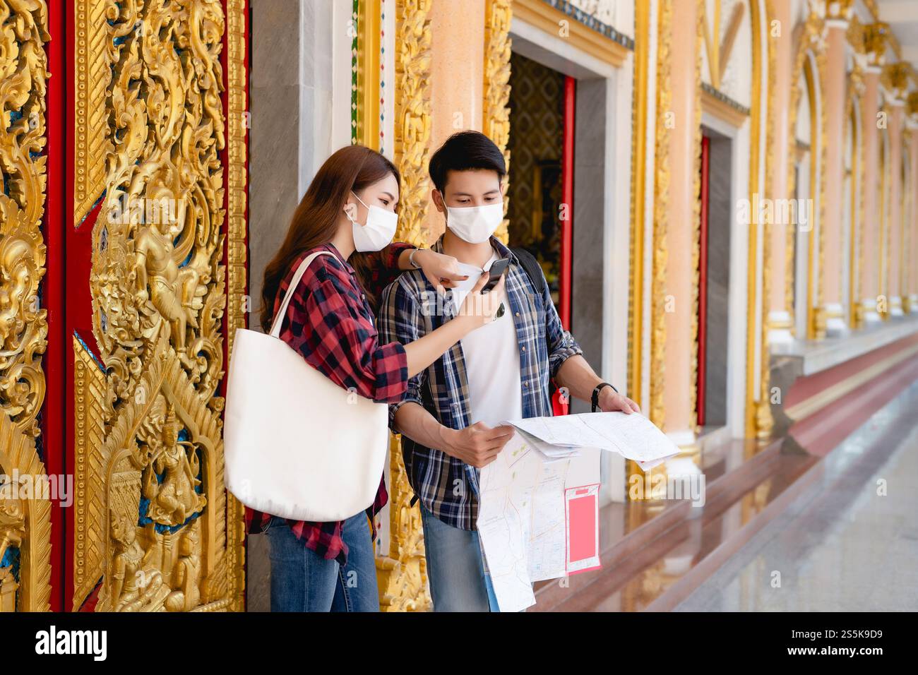 Smiley couple asiatique routards touristiques debout dans le beau temple thaïlandais, jolie femme tenant la carte de papier et bel homme check in smartphone avec Banque D'Images