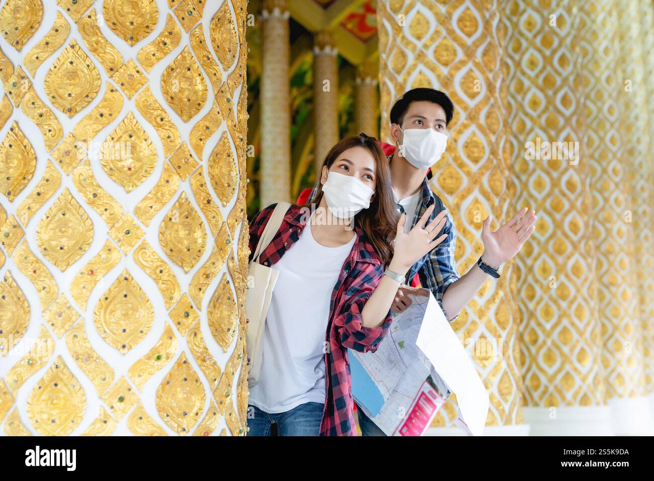 Portrait jeune couple de routards asiatiques debout et tiennent la carte de papier à la main au beau temple thaïlandais, ils agitent la main à la salutation et regardent vers l'avant Banque D'Images