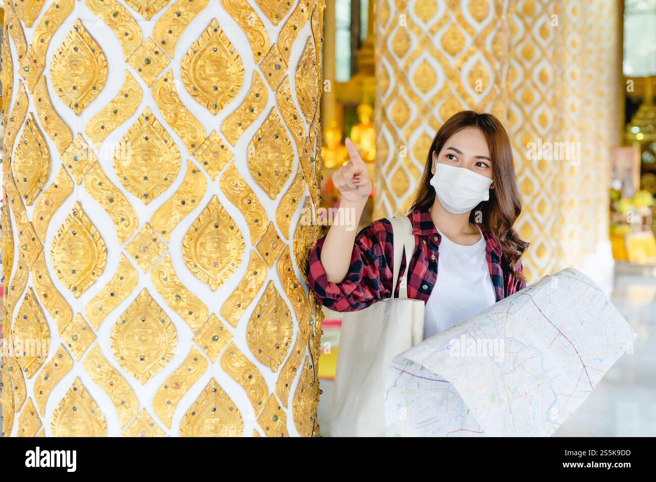 Portrait jeune femme de routard asiatique dans le masque debout et tenir la carte de papier à la main au beau temple thaïlandais, elle pointe et regarde vers l'avant Banque D'Images