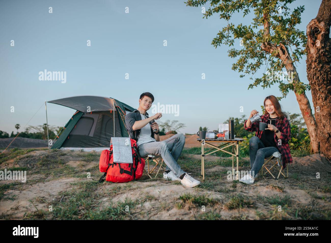 Joyeux couple jeune routard assis à l'avant de la tente dans la forêt avec set à café et faire moulin à café frais pendant le voyage de camping en été Banque D'Images