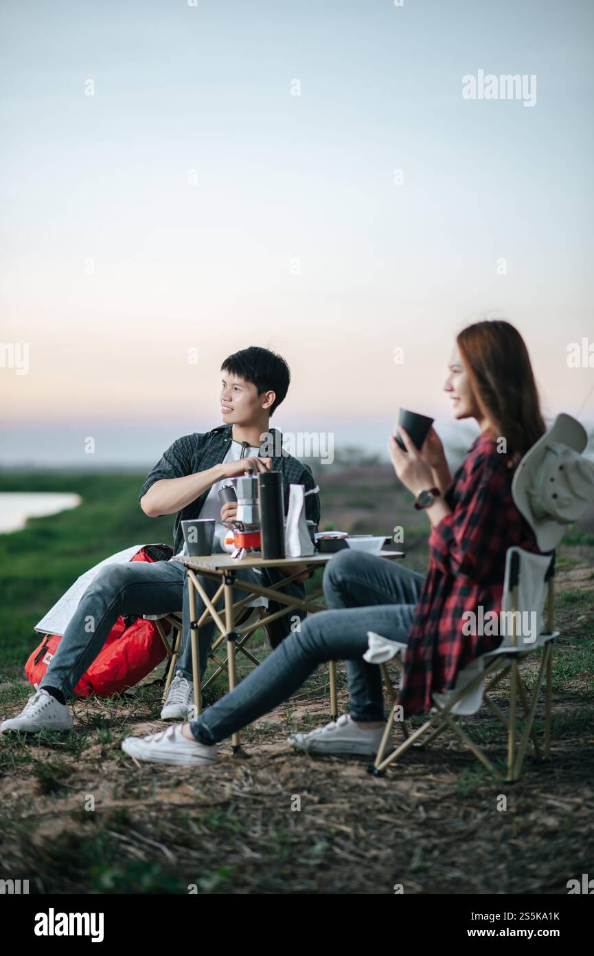 Mise au point sélective, bel homme faisant moulin à café frais, joyeux couple jeune routard assis devant la tente près du lac avec set de café Banque D'Images