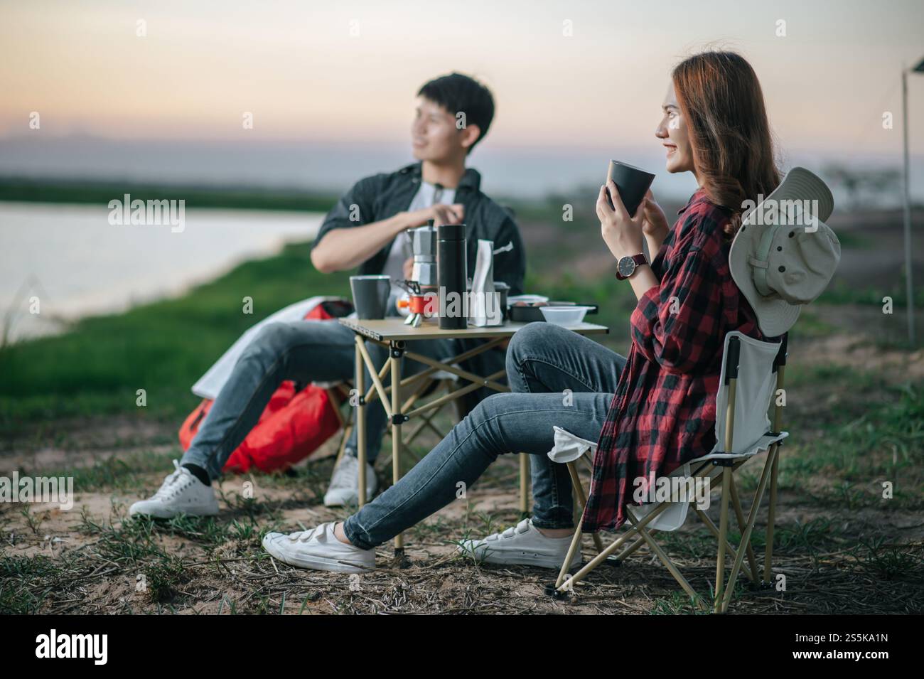 Joyeux couple jeune routard assis à l'avant de la tente dans la forêt avec set à café et faire moulin à café frais pendant le voyage de camping en été Banque D'Images