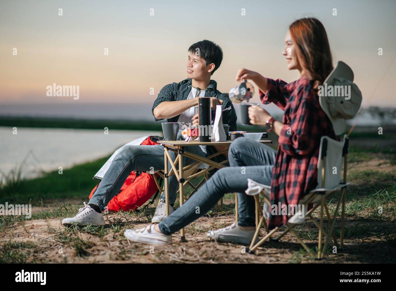 Joyeux couple jeune routard assis à l'avant de la tente dans la forêt avec set à café et faire moulin à café frais pendant le voyage de camping en été Banque D'Images
