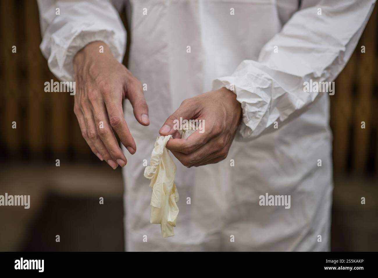 Fermez les mains d’un homme en costume d’équipement de protection individuelle (EPI) enlevant les gants après avoir travaillé pour enlever le covid-19. Banque D'Images