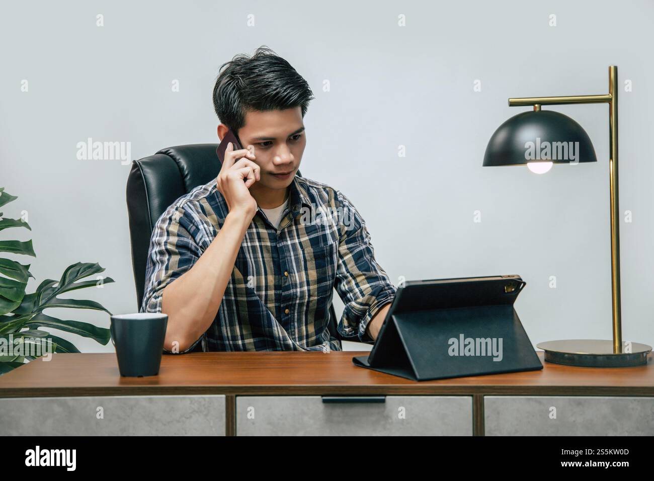 Jeune homme beau avec une nouvelle normalité, rester à la maison et travailler à partir de la maison sur tablette numérique et utiliser smartphone pendant l'auto-isolement et la quarantaine Banque D'Images