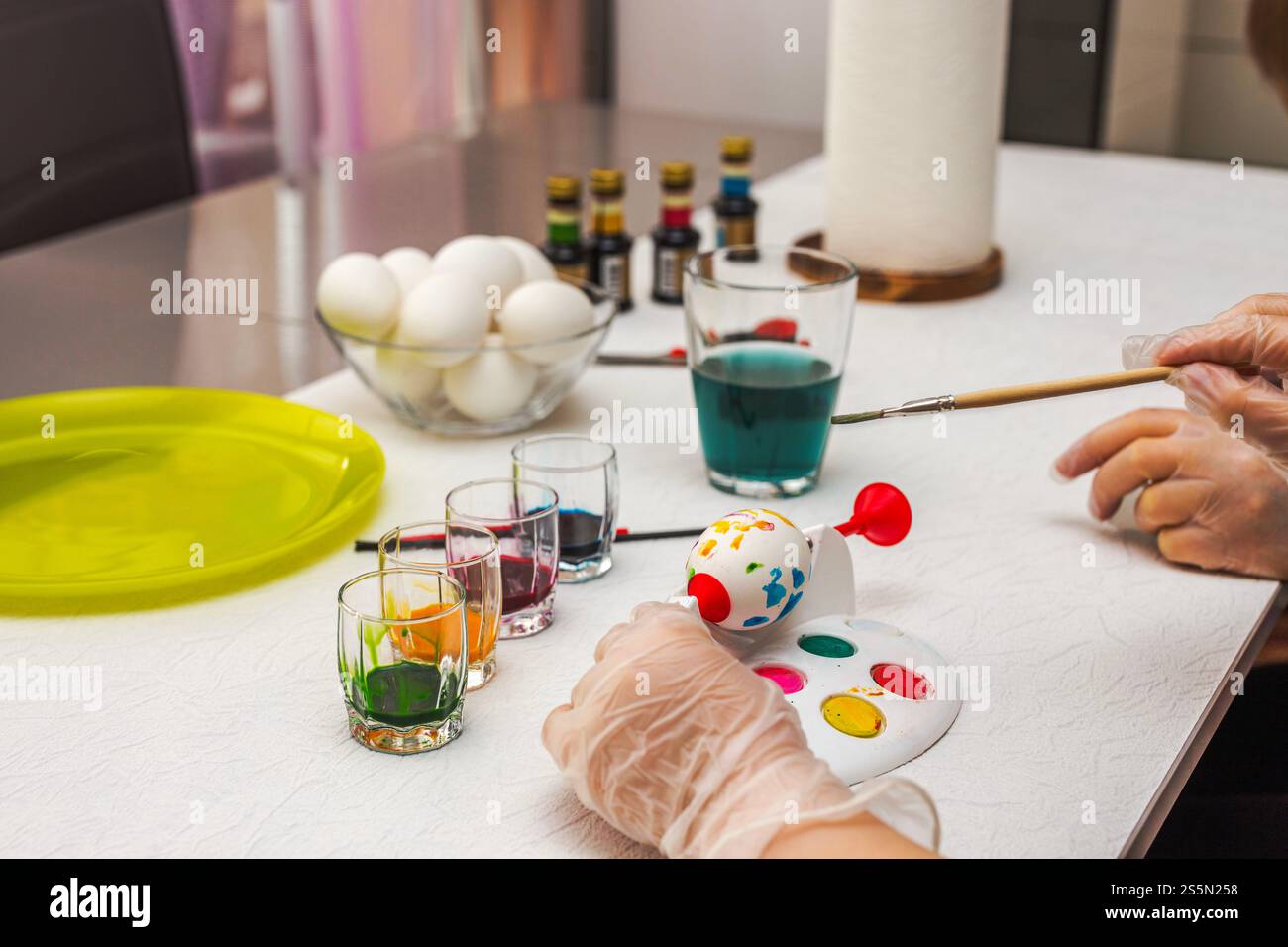 Mère enseignant à l'enfant de peindre l'oeuf de Pâques en utilisant un dispositif de peinture d'oeuf rotatif spécialisé avec des colorants colorés sur la table. Banque D'Images