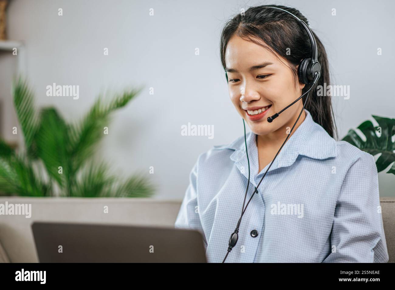 Jeune femme d'affaires travaillant sur l'ordinateur, parlant en ligne à l'aide d'un casque tout en étant assis sur le canapé confortable à la maison. Concept de télétravail à partir de Banque D'Images