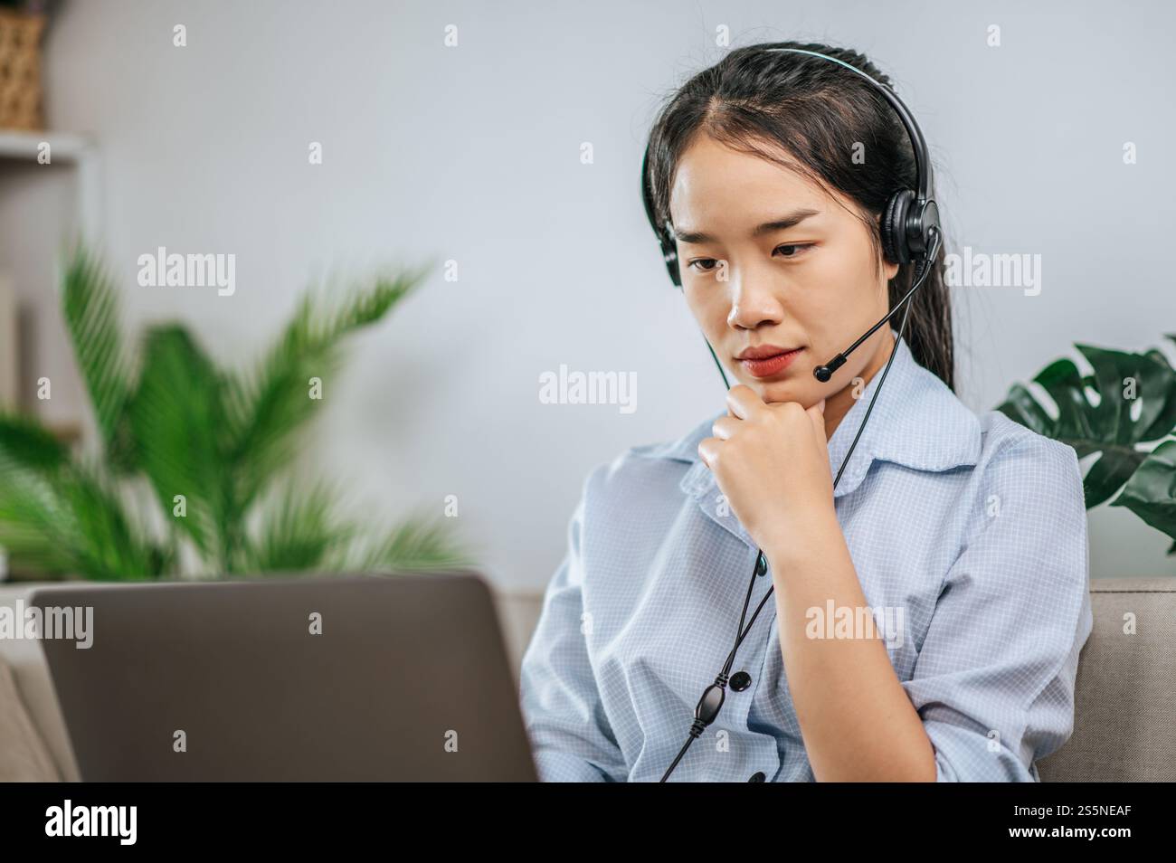 Jeune femme d'affaires travaillant sur l'ordinateur, parlant en ligne à l'aide d'un casque tout en étant assis sur le canapé confortable à la maison. Concept de télétravail à partir de Banque D'Images