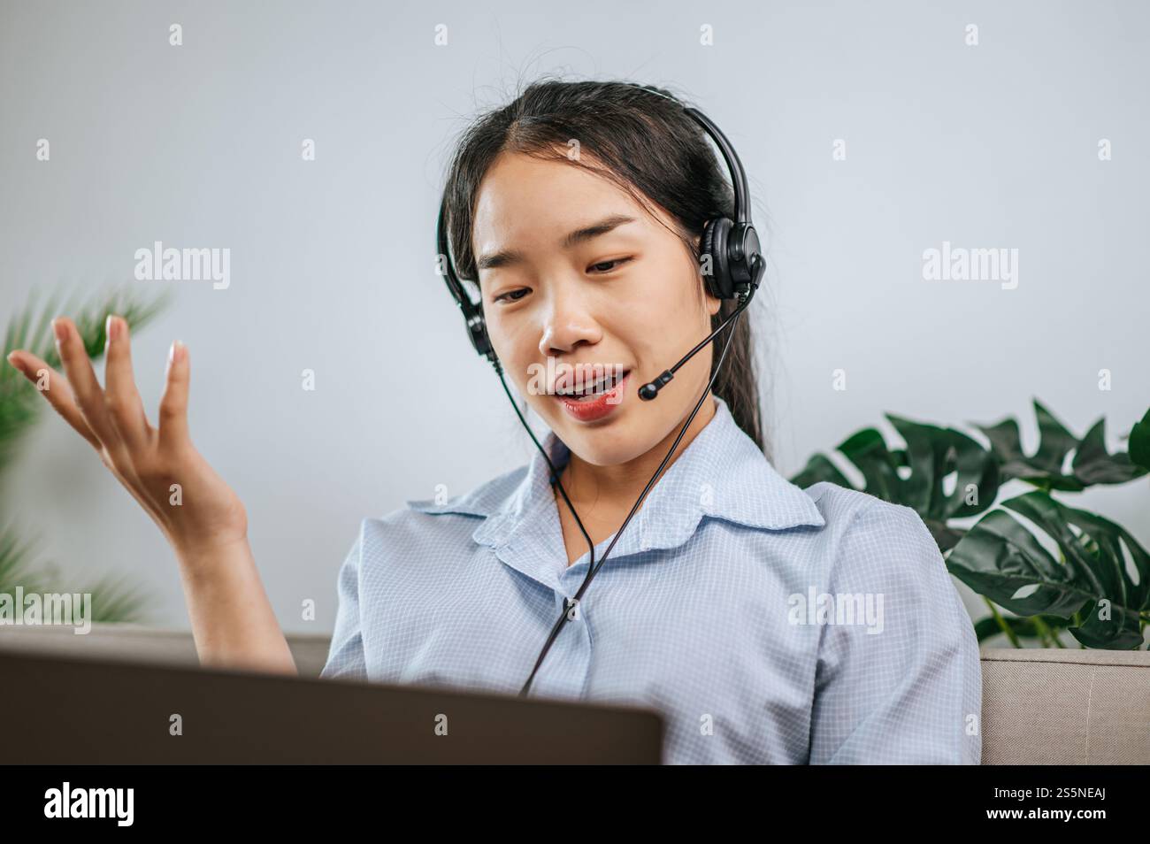 Jeune femme d'affaires travaillant sur l'ordinateur, parlant en ligne à l'aide d'un casque tout en étant assis sur le canapé confortable à la maison. Concept de télétravail à partir de Banque D'Images