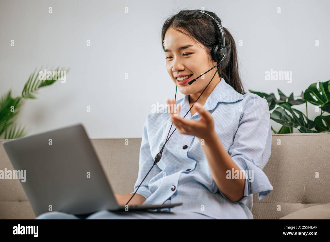 Jeune femme d'affaires travaillant sur l'ordinateur, parlant en ligne à l'aide d'un casque tout en étant assis sur le canapé confortable à la maison. Concept de télétravail à partir de Banque D'Images