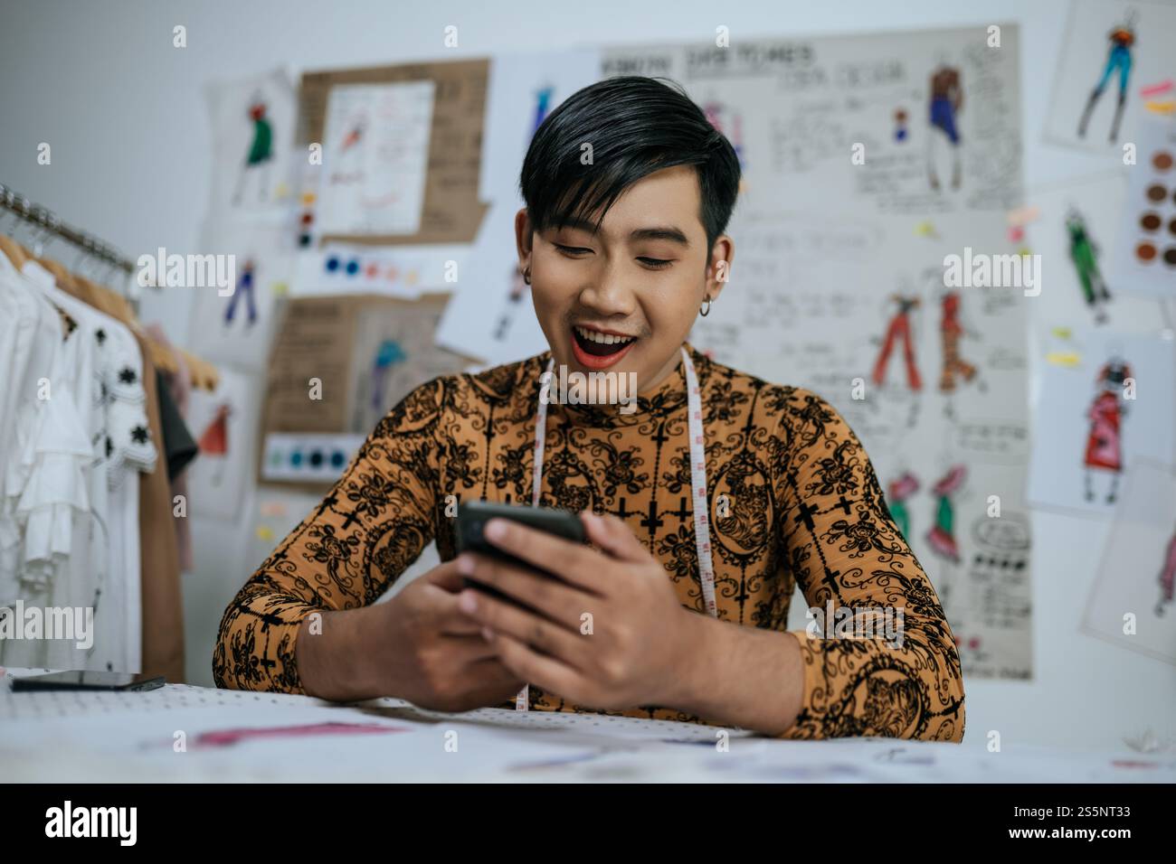 Portrait de professionnel asiatique jeune tailleur masculin avec ruban à mesurer sur le cou en utilisant sur smartphone avec fond de dessins en studio. Concepteur et Banque D'Images