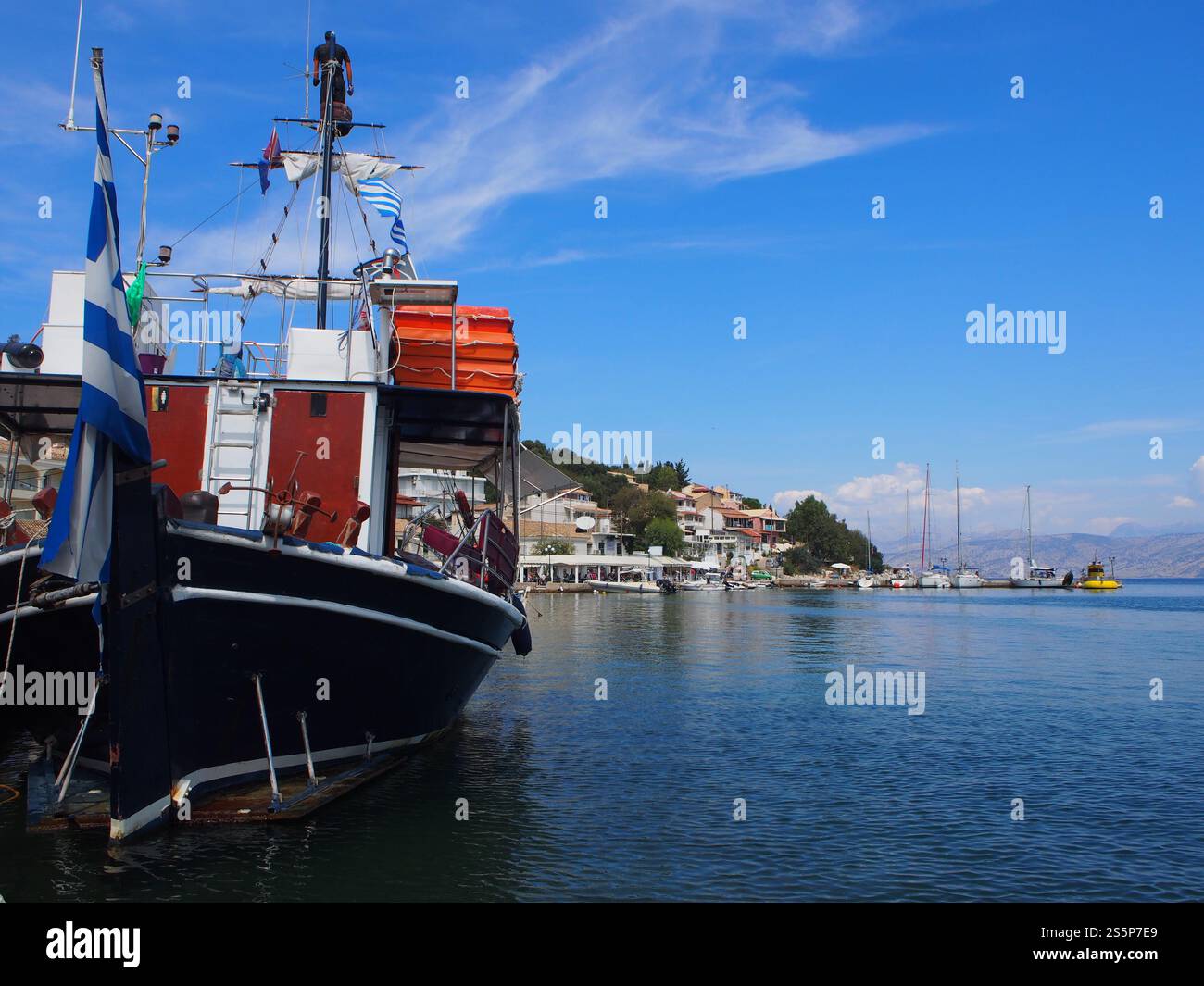 Un bateau a accosté sur un quai dans une baie de Corfou (Kerkyra), Grèce avec des maisons et d'autres bateaux alignés en arrière-plan Banque D'Images