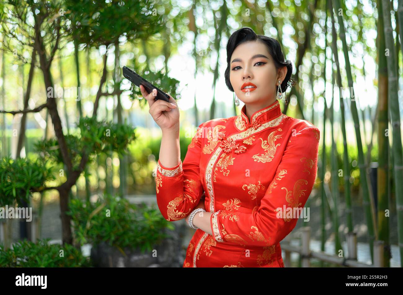 Portrait jolie femme asiatique dans un cheongsam chinois posant avec smartphone sur fond de forêt de bambou, espace de copie, concept du nouvel an chinois Banque D'Images