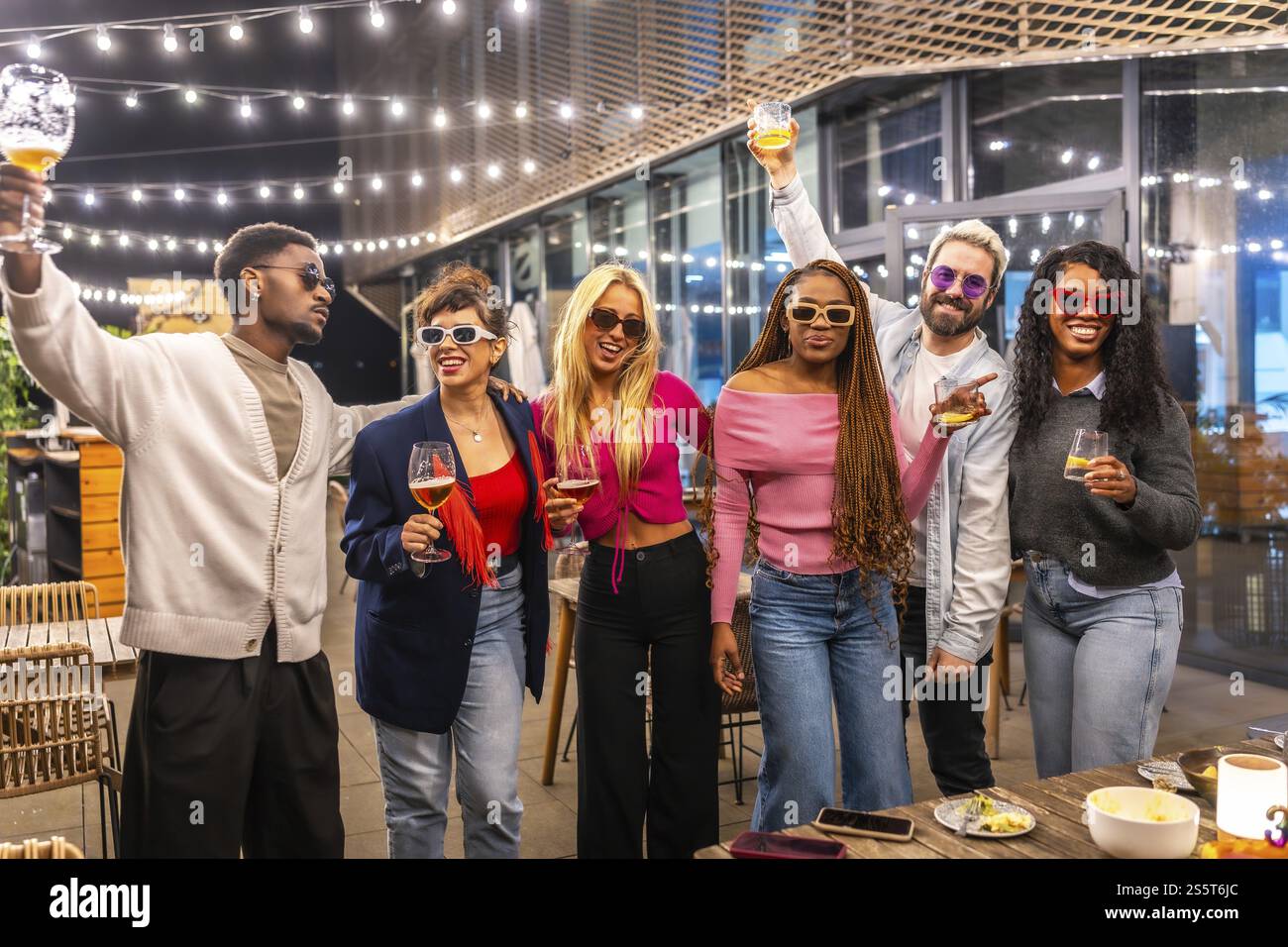 Amis multiethniques levant des verres célébrant la fête le soir sur la terrasse d'un bar moderne Banque D'Images