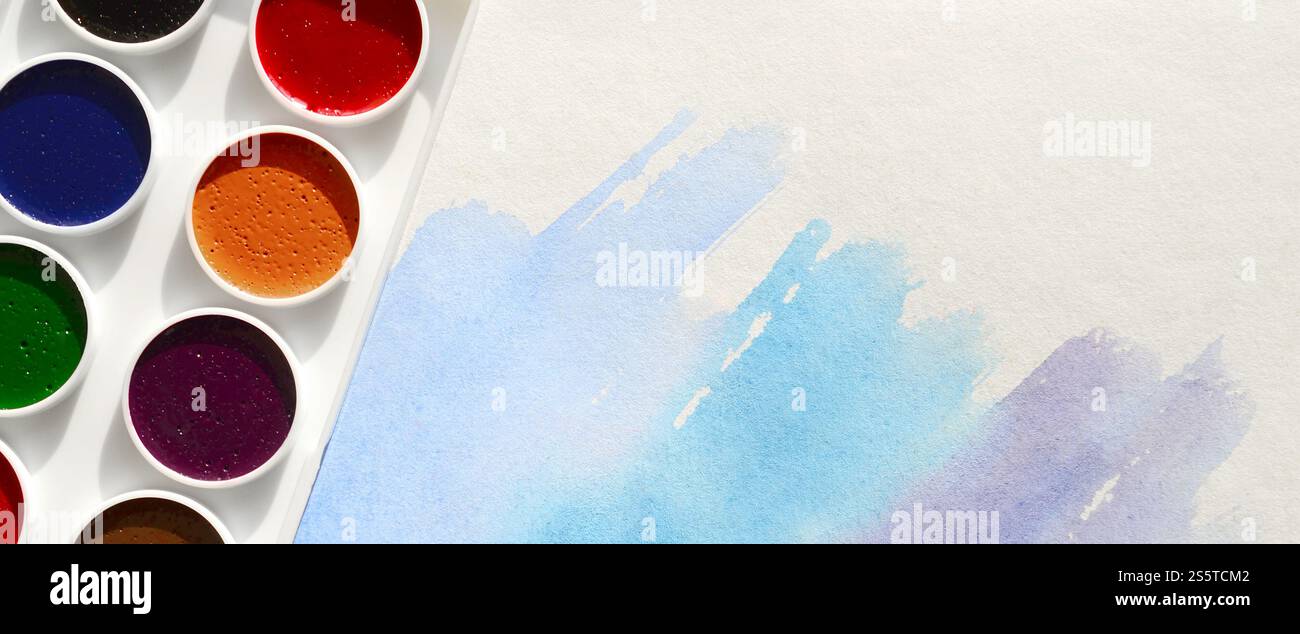 Un nouvel ensemble d'aquarelles repose sur une feuille de papier, qui montre un dessin abstrait d'aquarelle sous la forme de traits bleus. Le concept d'amateur Banque D'Images