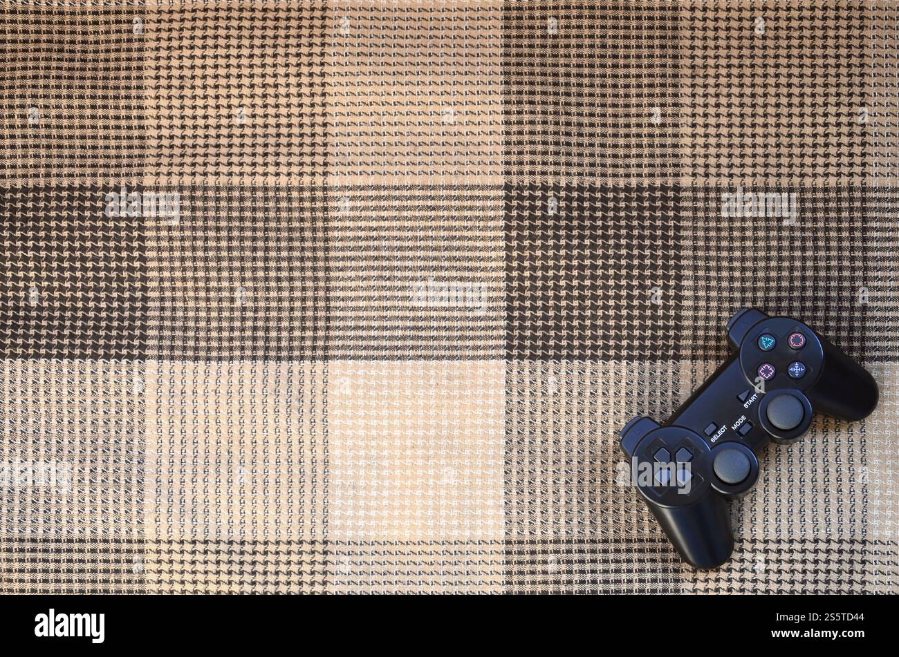 Le contrôleur de jeu vidéo de la console de jeu est sur le canapé à carreaux. Dispositif sans fil de commande pendant des jeux vidéo. Dispositif de commande de jeu vidéo Banque D'Images
