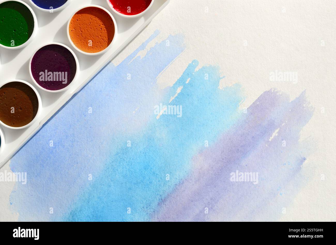 Un nouvel ensemble d'aquarelles repose sur une feuille de papier, qui montre un dessin abstrait d'aquarelle sous la forme de traits bleus. Le concept d'amateur Banque D'Images