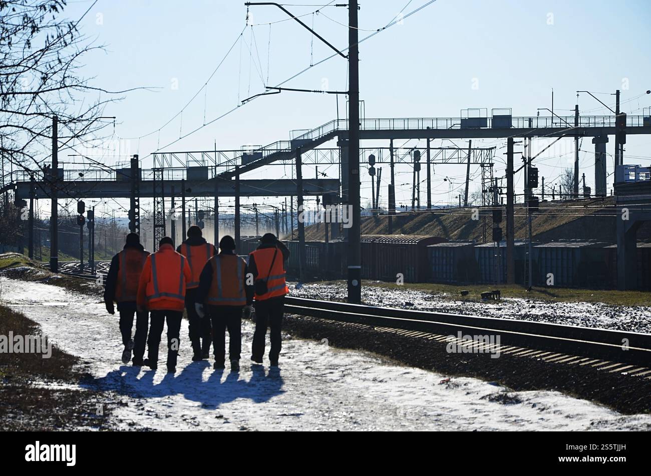 Plusieurs cheminots en signalant des uniformes orange sales sont sur la route à côté de la ligne de chemin de fer. L'équipe du train se rend au travail en hiver ensoleillé Banque D'Images Plusieurs cheminots en signalant des uniformes orange sales sont sur la route à côté de la ligne de chemin de fer. L'équipe du train se rend au travail en hiver ensoleillé Banque D'Images