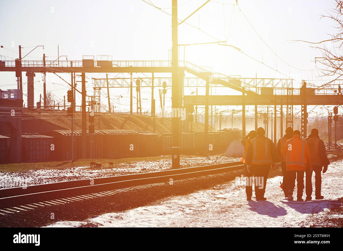 Plusieurs cheminots en signalant des uniformes orange sales sont sur la route à côté de la ligne de chemin de fer. L'équipe du train se rend au travail en hiver ensoleillé Banque D'Images