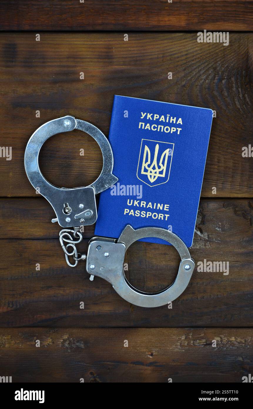 Un passeport ukrainien avec les menottes de la police se trouve sur une table en bois. Des problèmes avec la loi durant la traversée des frontières du pays. Le commerce illégal Banque D'Images