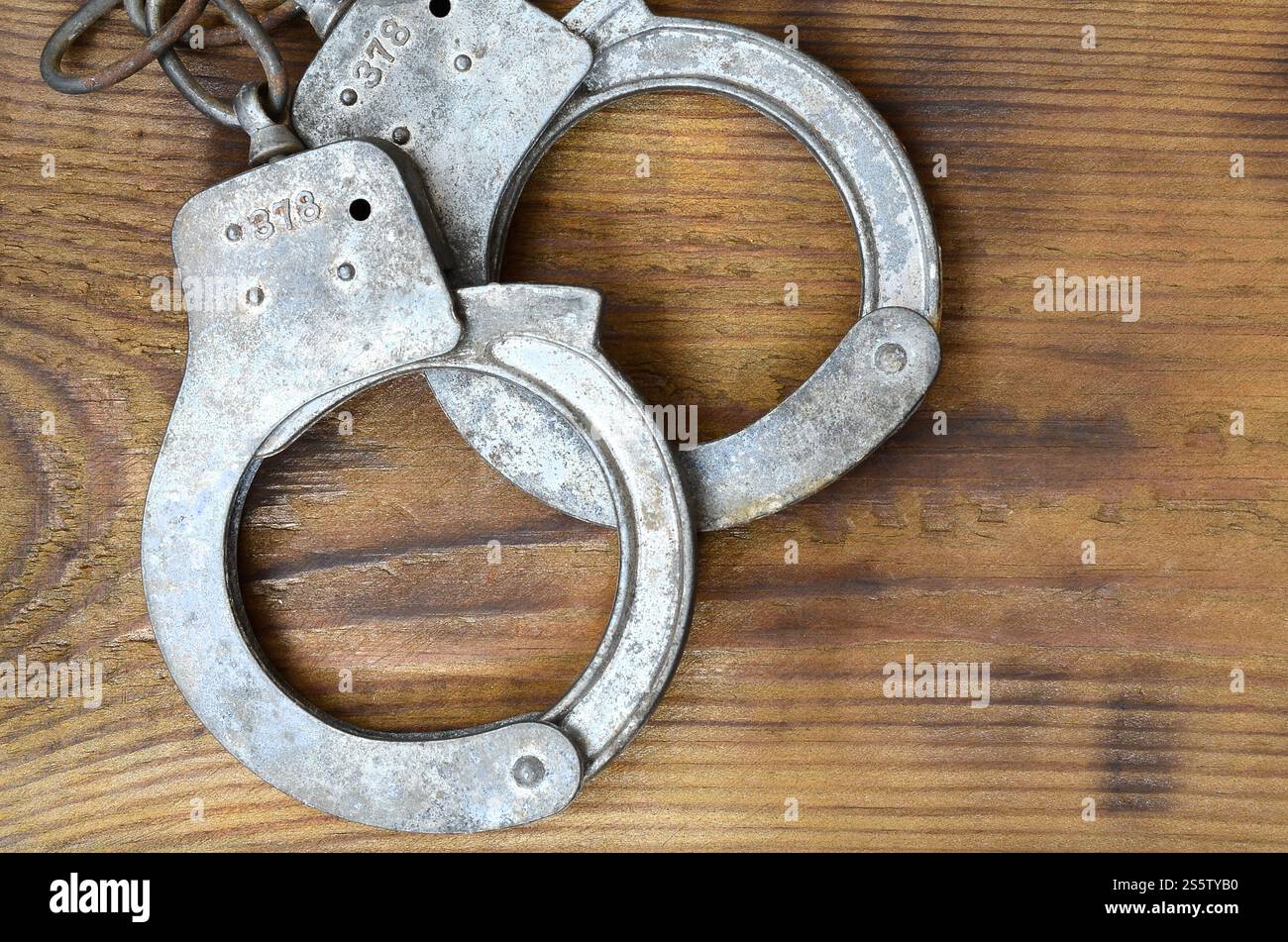 Les menottes de police vieilles et rouillées reposent sur une surface en bois rayée. Le concept d'un vieux crime Banque D'Images