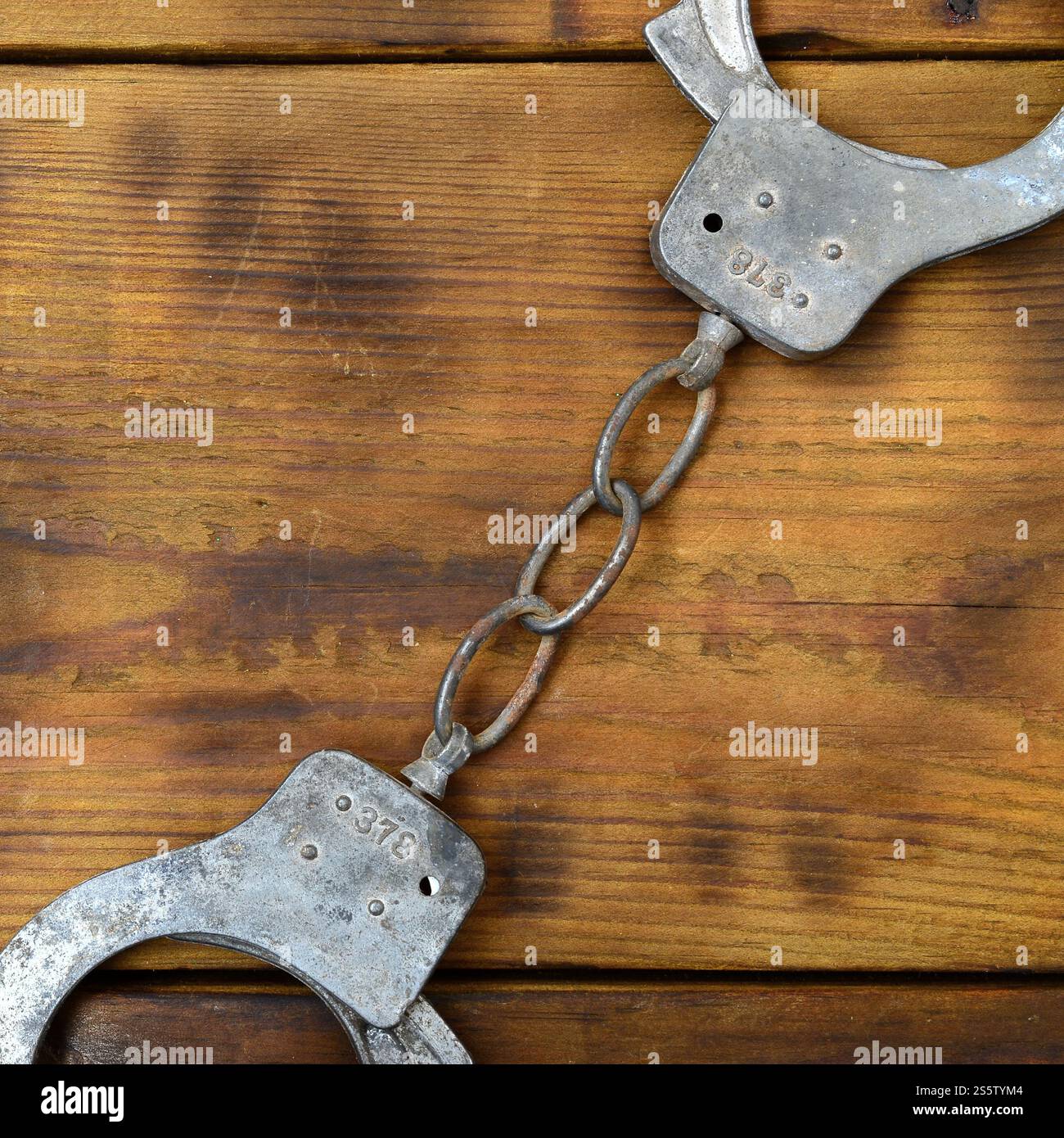 Les menottes de police vieilles et rouillées reposent sur une surface en bois rayée. Le concept d'un vieux crime Banque D'Images