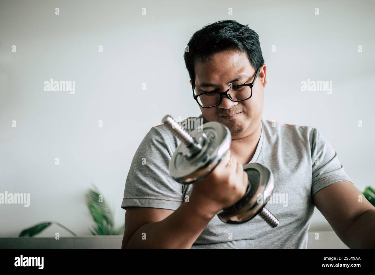 Jeune homme de graisse asiatique dans des lunettes soulevant l'haltère pour exercer pour un espace sain et copiant Banque D'Images