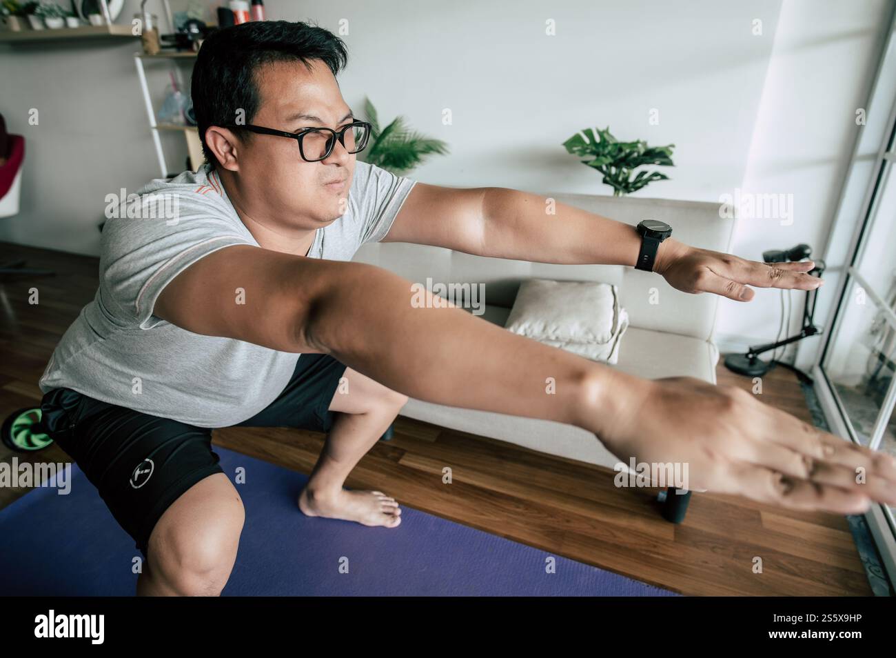 Drôle homme en surpoids faisant squats statiques brûlant les graisses, sur tapis de sport dans l'exercice du salon pour un espace de copie sain Banque D'Images
