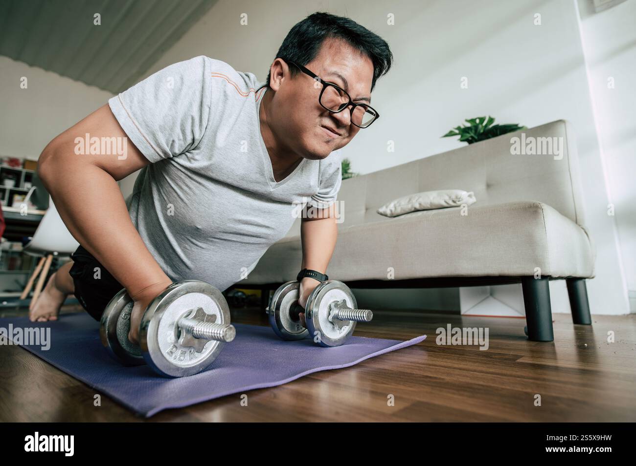 Homme drôle en surpoids faisant la combustion des graisses d'entraînement sur le tapis de sport avec des haltères dans la pose push-up dans le salon, exercice pour un espace de copie sain Banque D'Images