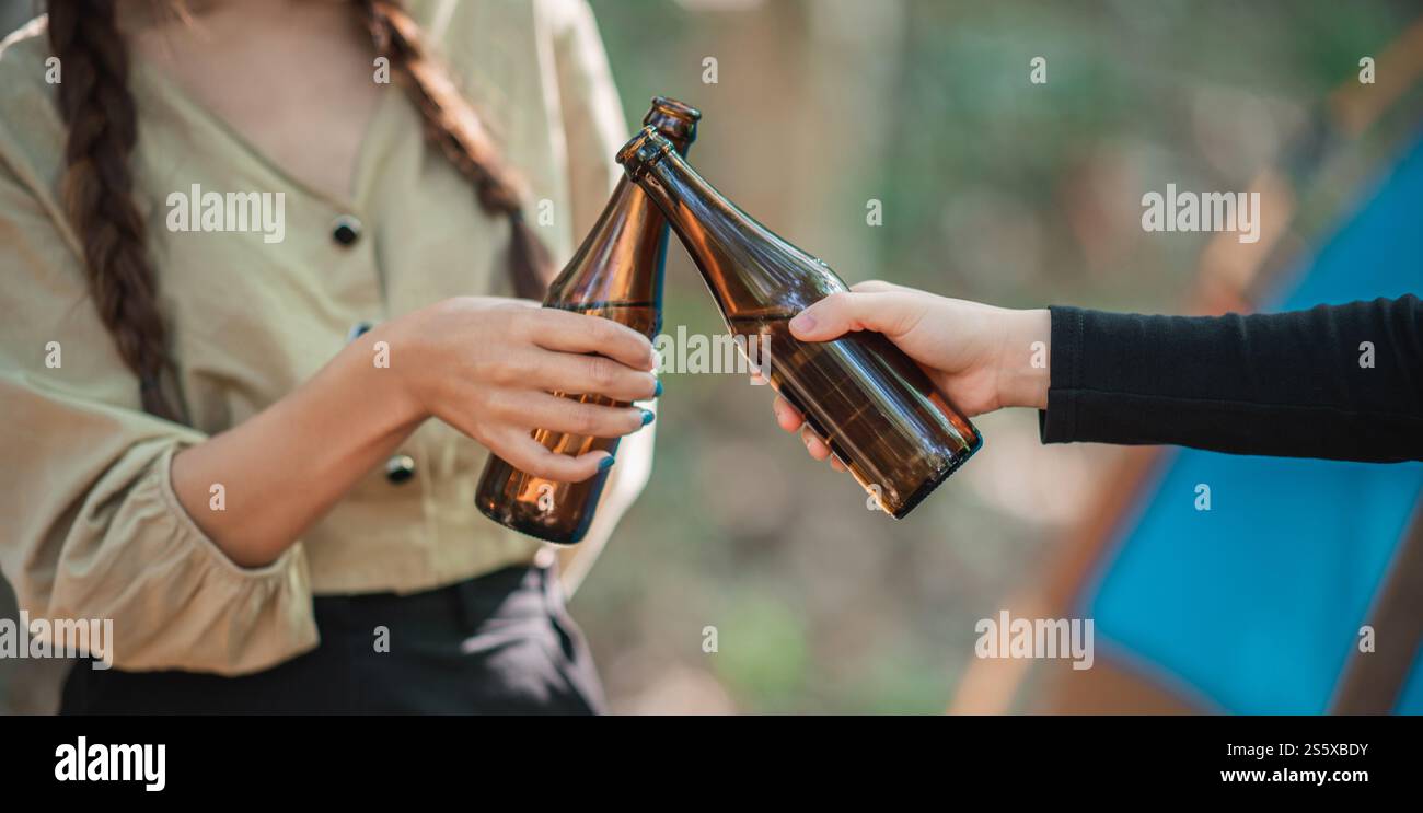 Gros plan et mise au point sélective, mains de belle femme asiatique et amical stravelers tenant des bières en bouteille et acclamant tout en se relaxant devant Banque D'Images