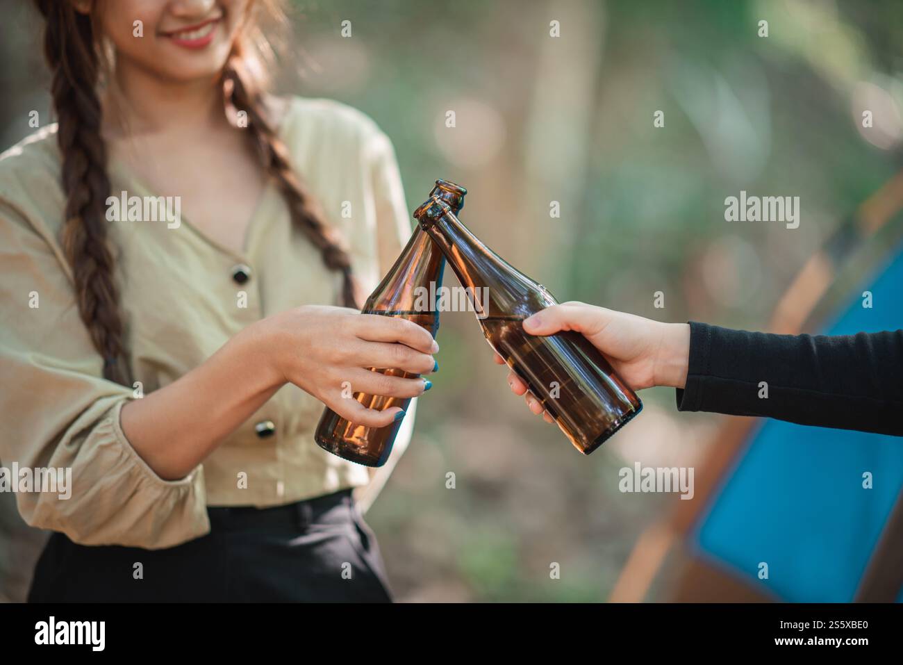 Gros plan et mise au point sélective, mains de belle femme asiatique et amical stravelers tenant des bières en bouteille et acclamant tout en se relaxant devant Banque D'Images