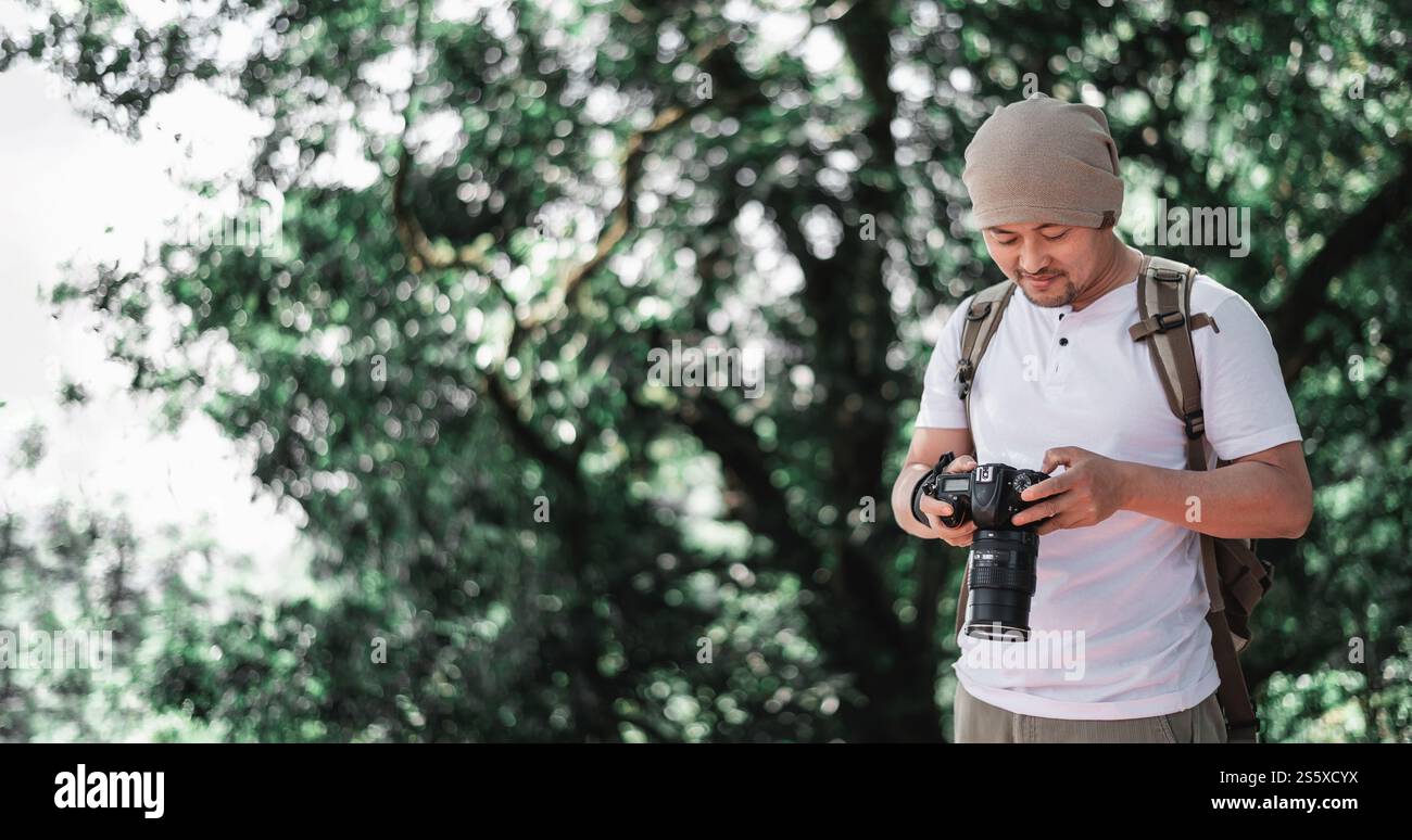 Homme de voyage asiatique avec sac à dos vérifiant une image sur la caméra au parc avec espace de copie. Photographe de voyage. Vocation et concept de vacances. Banque D'Images