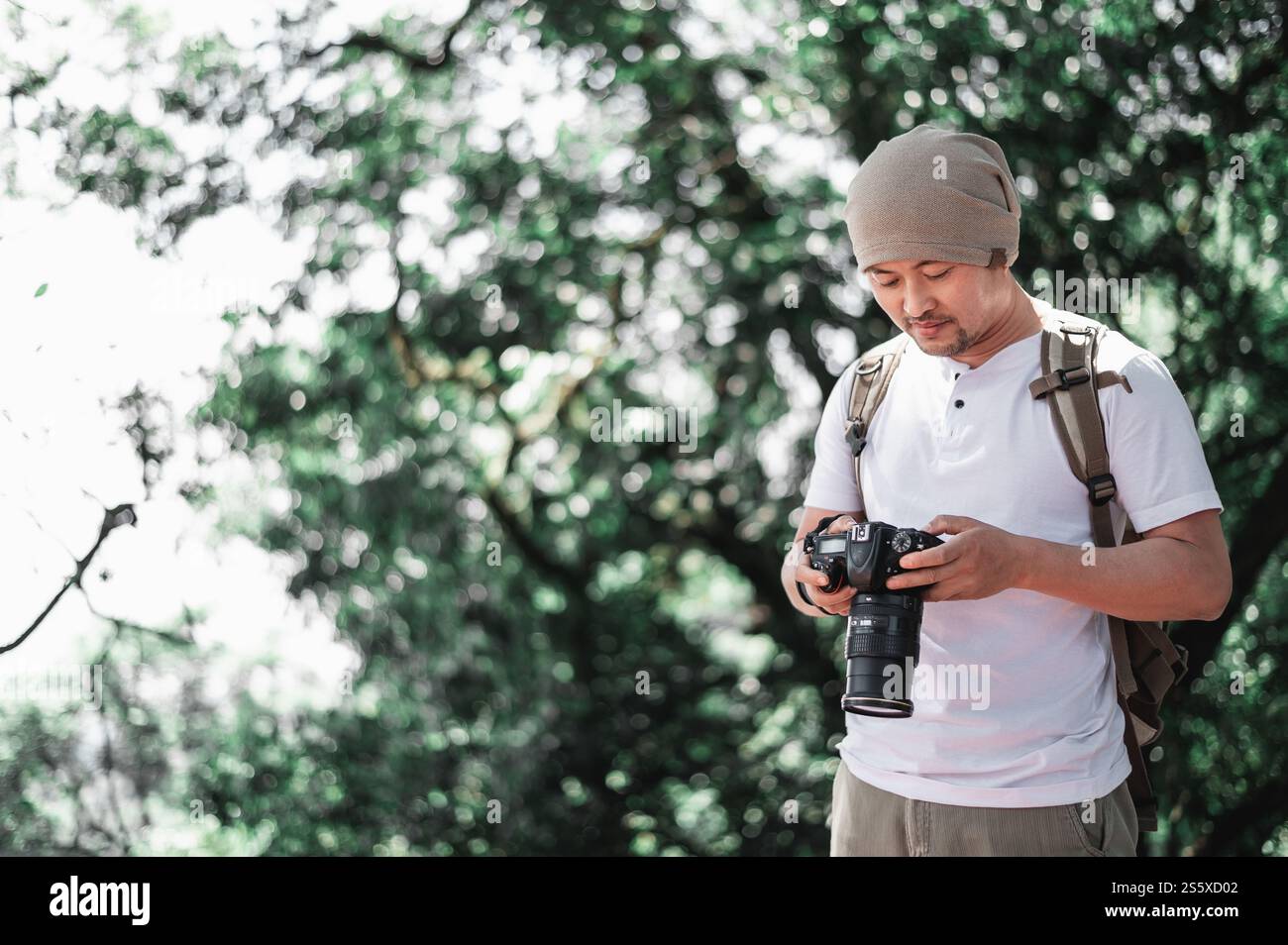 Homme de voyage asiatique avec sac à dos vérifiant une image sur la caméra au parc avec espace de copie. Photographe de voyage. Vocation et concept de vacances. Banque D'Images