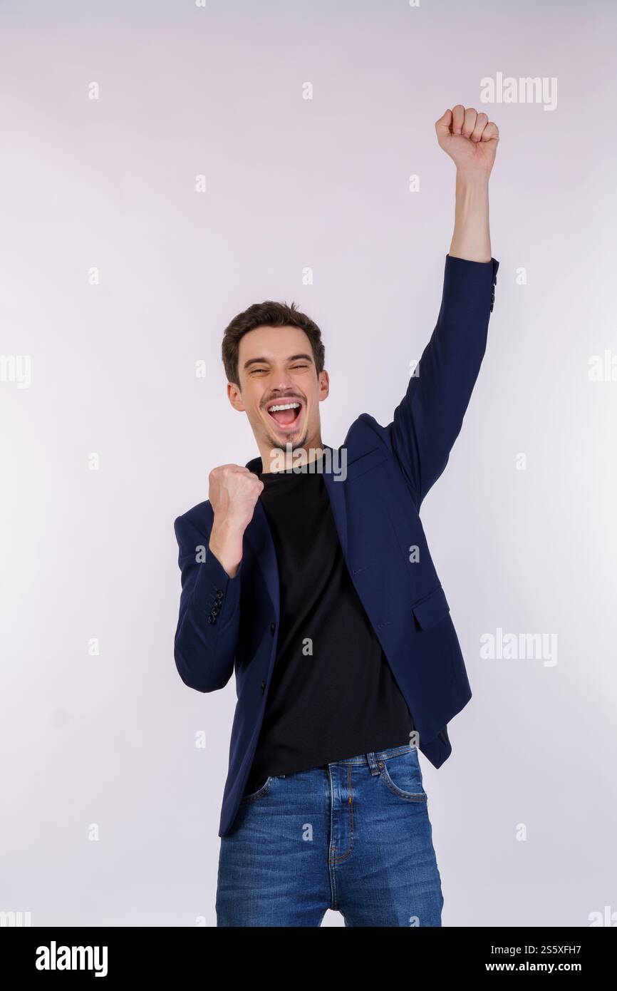 Portrait d'heureux joyeux jeune homme d'affaires debout faisant le geste gagnant serrant les poings gardant isolé sur le studio de fond de mur de couleur blanche. Banque D'Images