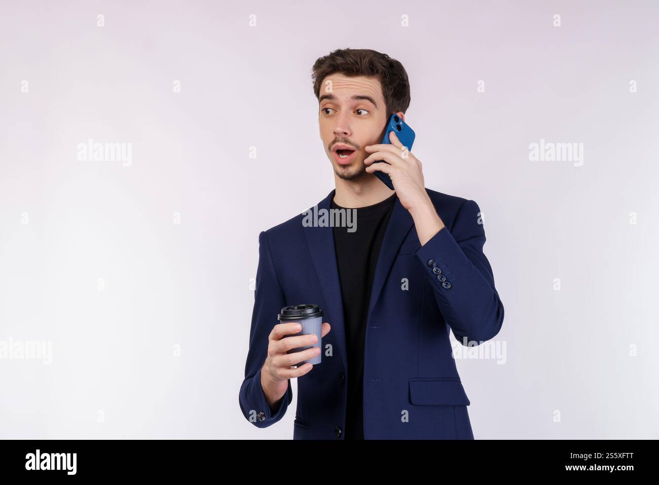 Portrait de beau homme d'affaires choqué parlant par téléphone portable et tenant le café chaud isolé sur fond blanc. Banque D'Images