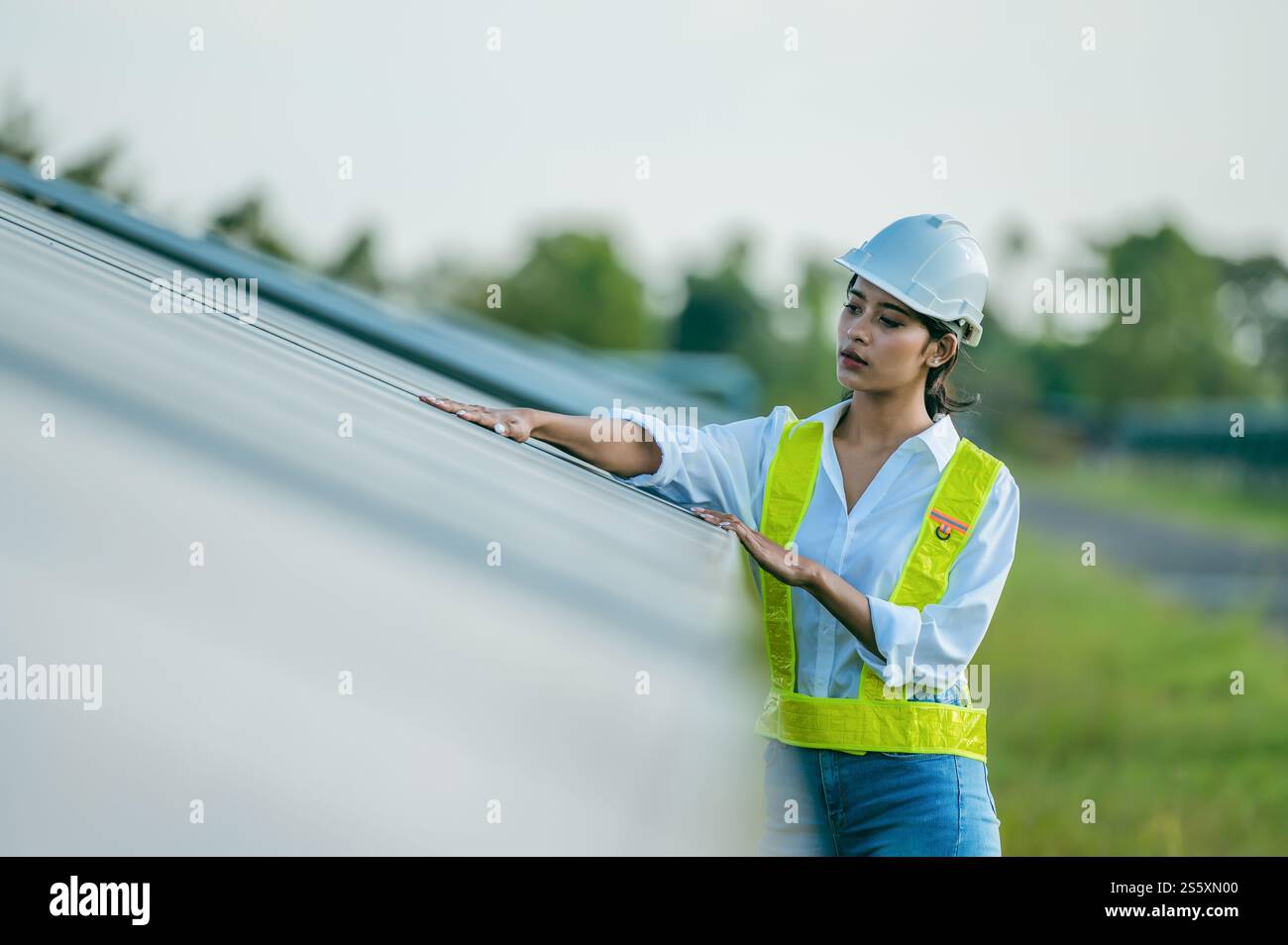 Portrait asiatique jeune femme ingénieur portant des vêtements de protection et casque blanc debout près de panneaux solaires tout en travaillant dans la ferme solaire, à la recherche Banque D'Images