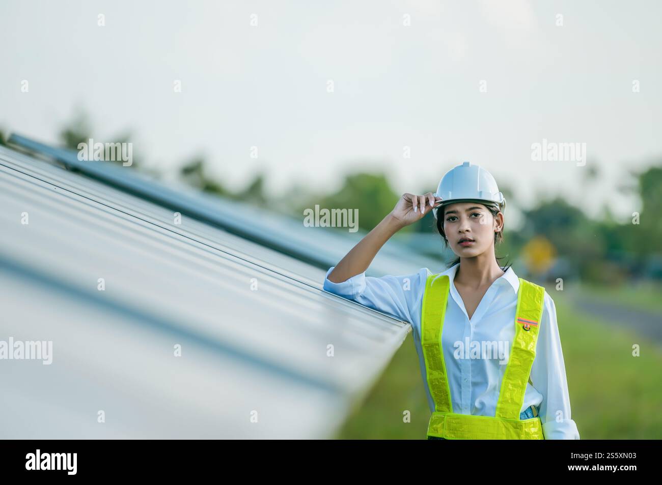 Portrait asiatique jeune femme ingénieur portant des vêtements de protection et casque blanc debout près de panneaux solaires tout en travaillant dans la ferme solaire, à la recherche Banque D'Images
