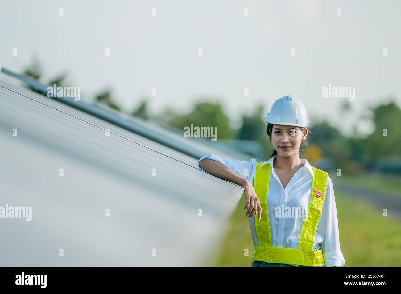 Portrait asiatique jeune femme ingénieur portant des vêtements de protection et casque blanc debout près de panneaux solaires tout en travaillant dans la ferme solaire, à la recherche Banque D'Images