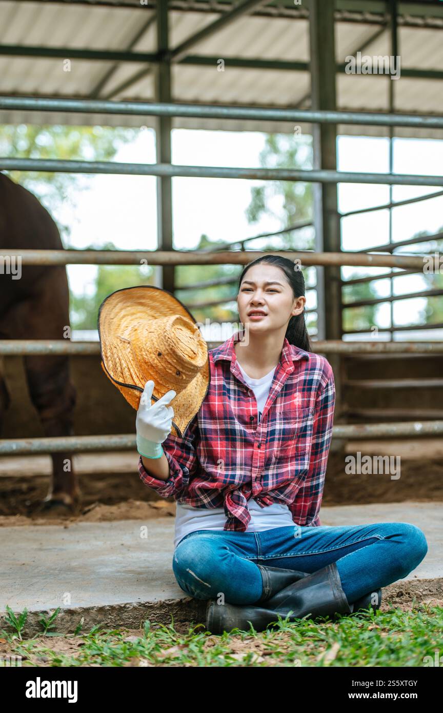 Portrait de jeune agricultrice asiatique fatiguée assise sur le sol dans l'étable. Industrie agricole, agriculture, personnes, technologie et élevage Banque D'Images