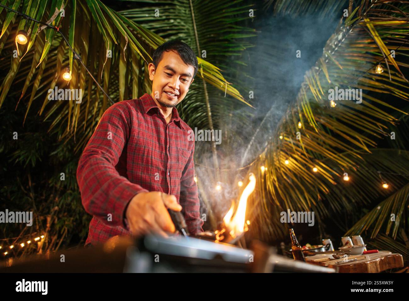 Portrait de jeune homme asiatique heureux cuisinant de la viande sur barbecue à la fête du nouvel an. Bar-B-Q ou BBQ sur poêle traditionnel. Soirée, personnes et Banque D'Images Portrait de jeune homme asiatique heureux cuisinant de la viande sur barbecue à la fête du nouvel an. Bar-B-Q ou BBQ sur poêle traditionnel. Soirée, personnes et Banque D'Images