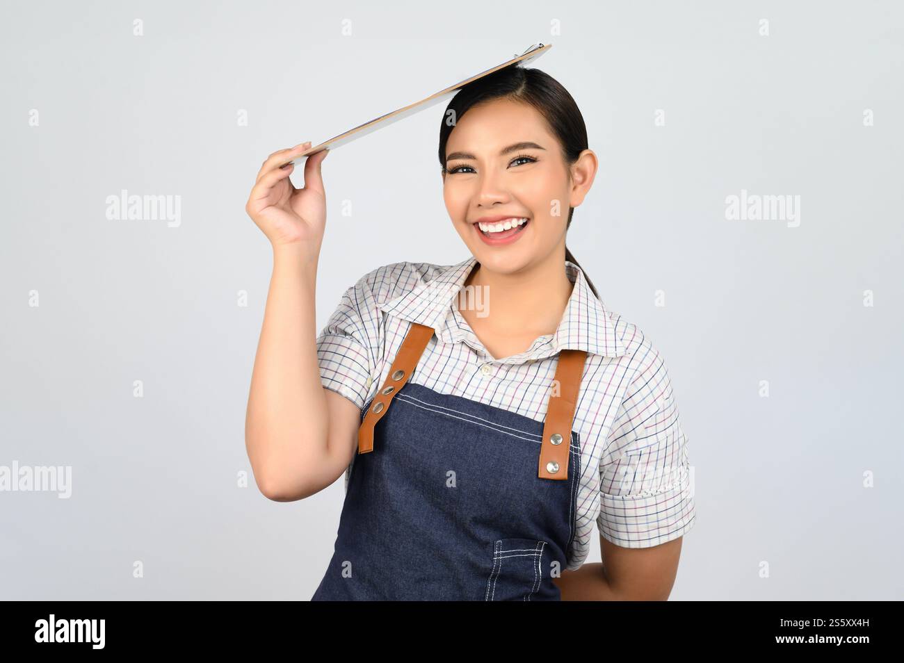 Portrait de jeune femme asiatique dans l'uniforme de serveuse tenant le presse-papiers sur la tête, copier l'espace pour insérer des produits pour la publicité isolé sur blanc Banque D'Images