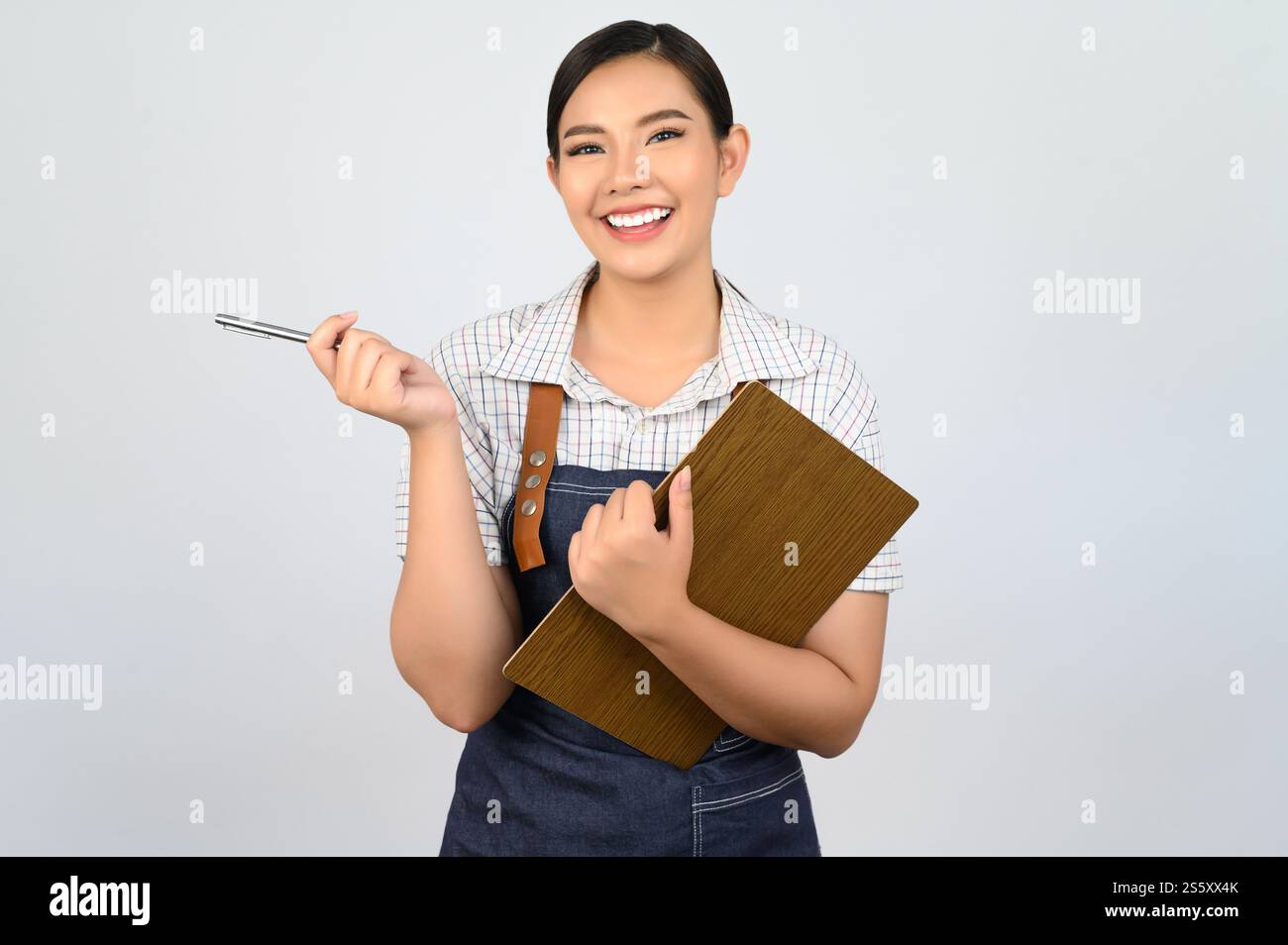 Portrait de jeune femme asiatique dans l'uniforme de serveuse tenant presse-papiers et stylo pour vérifier l'ordre, copier l'espace pour insérer des produits pour la publicité Banque D'Images