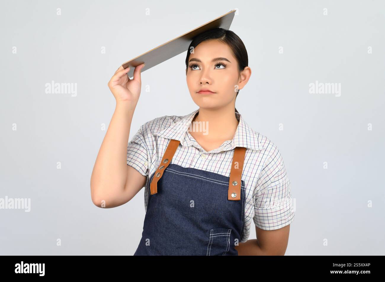 Portrait de jeune femme asiatique dans l'uniforme de serveuse tenant le presse-papiers sur la tête, copier l'espace pour insérer des produits pour la publicité isolé sur blanc Banque D'Images