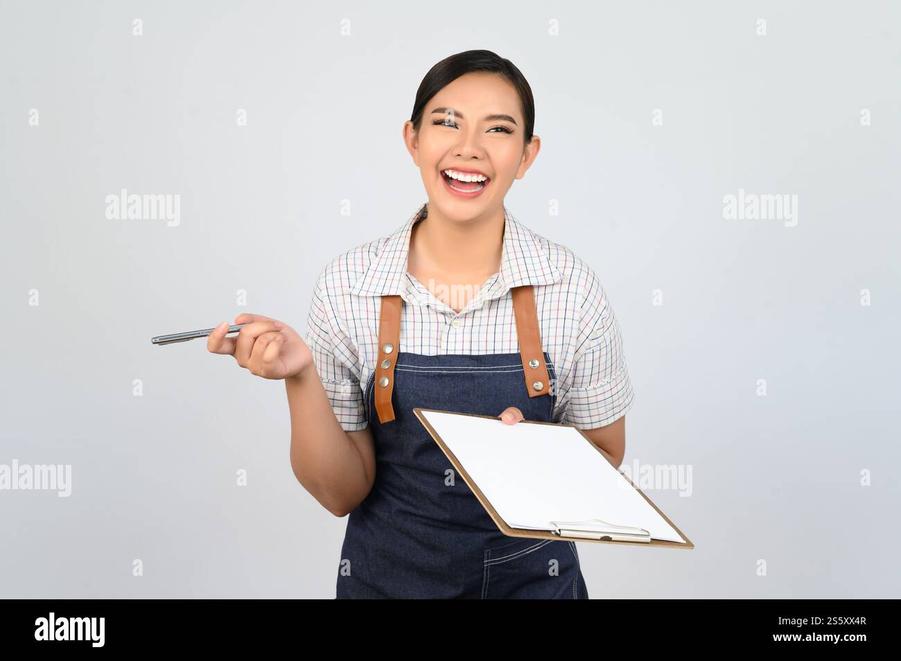 Portrait de jeune femme asiatique en uniforme de serveuse tenant maquette de presse-papiers avec stylo, espace de copie pour insérer du texte pour la publicité isolé sur blanc Banque D'Images