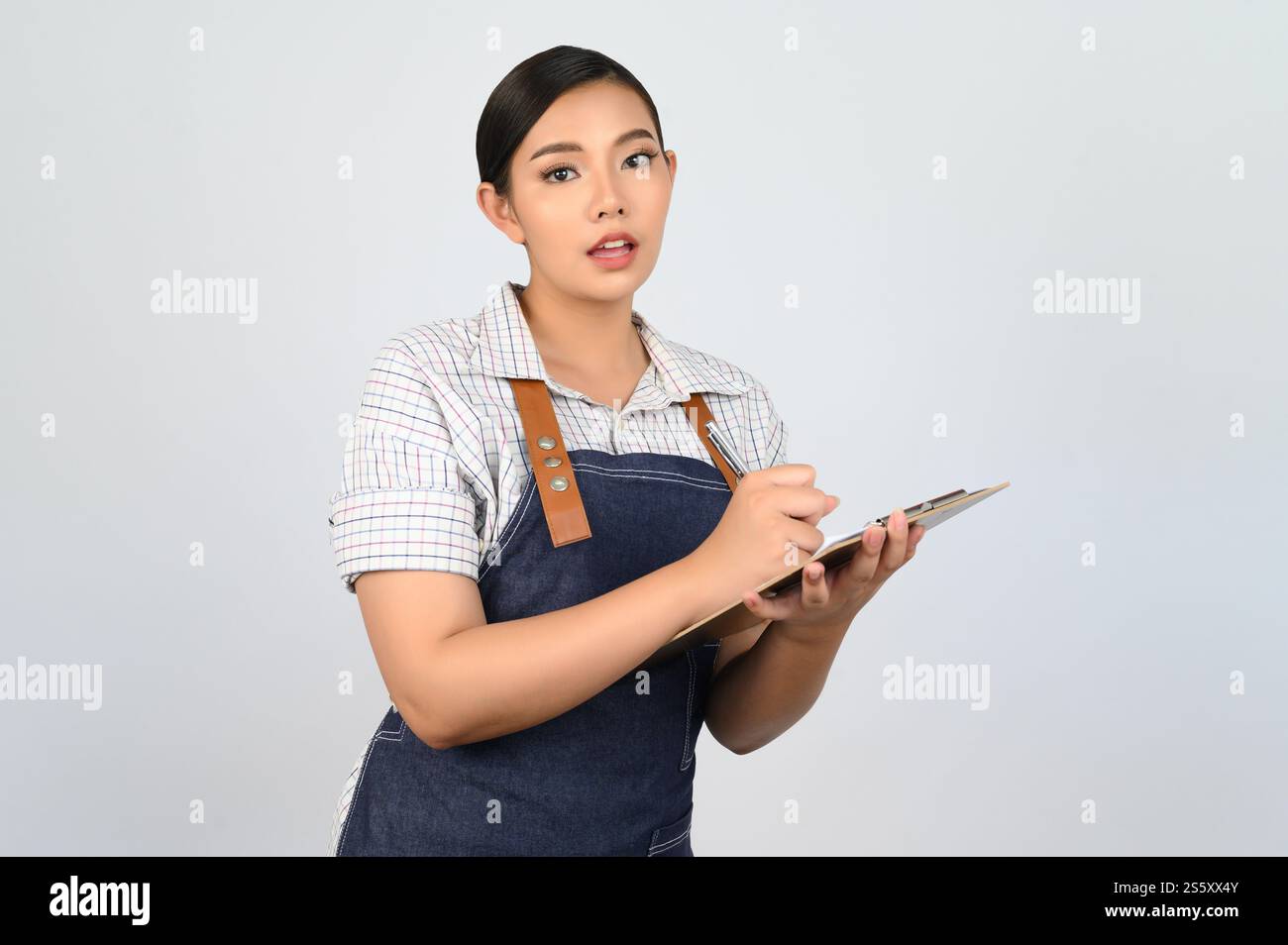 Portrait de jeune femme asiatique dans l'uniforme de serveuse tenant presse-papiers et stylo pour vérifier l'ordre, copier l'espace pour insérer des produits pour la publicité Banque D'Images