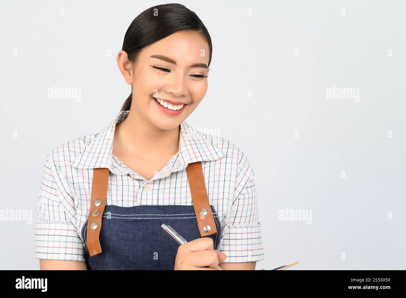 Portrait de jeune femme asiatique dans l'uniforme de serveuse tenant presse-papiers et stylo pour vérifier l'ordre, copier l'espace pour insérer des produits pour la publicité Banque D'Images