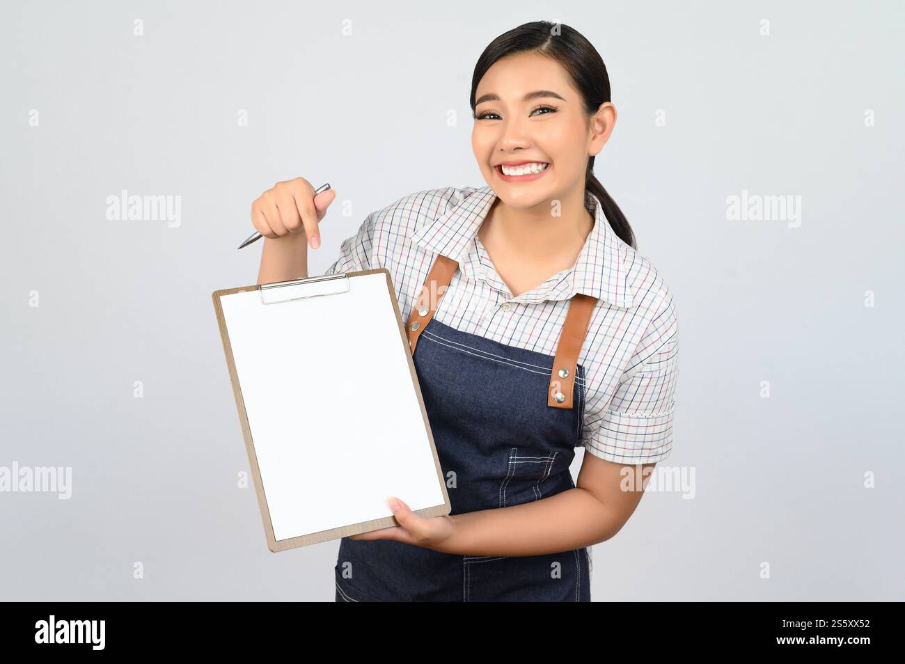 Portrait de jeune femme asiatique en uniforme de serveuse tenant maquette de presse-papiers avec stylo, espace de copie pour insérer du texte pour la publicité isolé sur blanc Banque D'Images