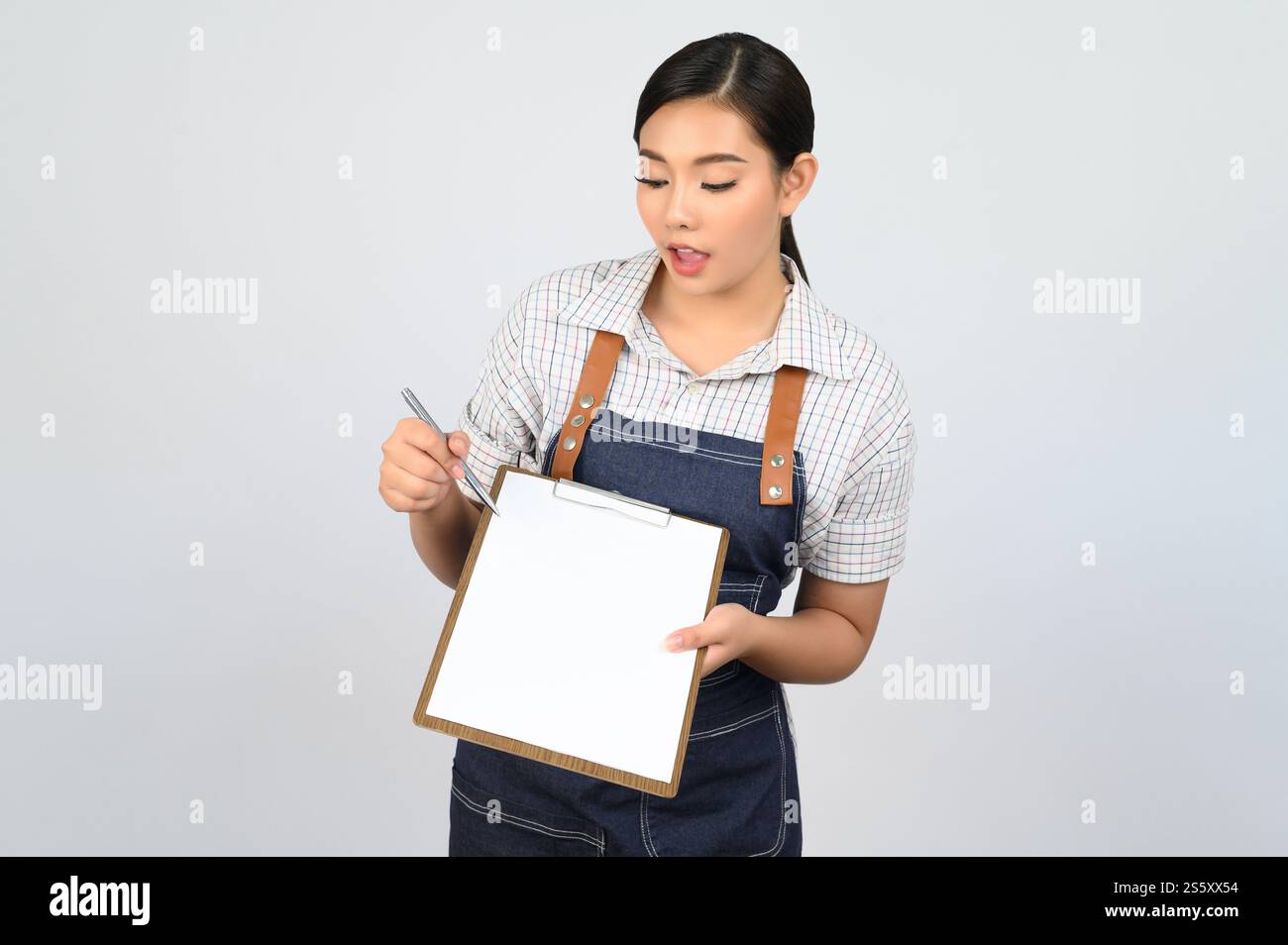Portrait de jeune femme asiatique en uniforme de serveuse tenant maquette de presse-papiers avec stylo, espace de copie pour insérer du texte pour la publicité isolé sur blanc Banque D'Images