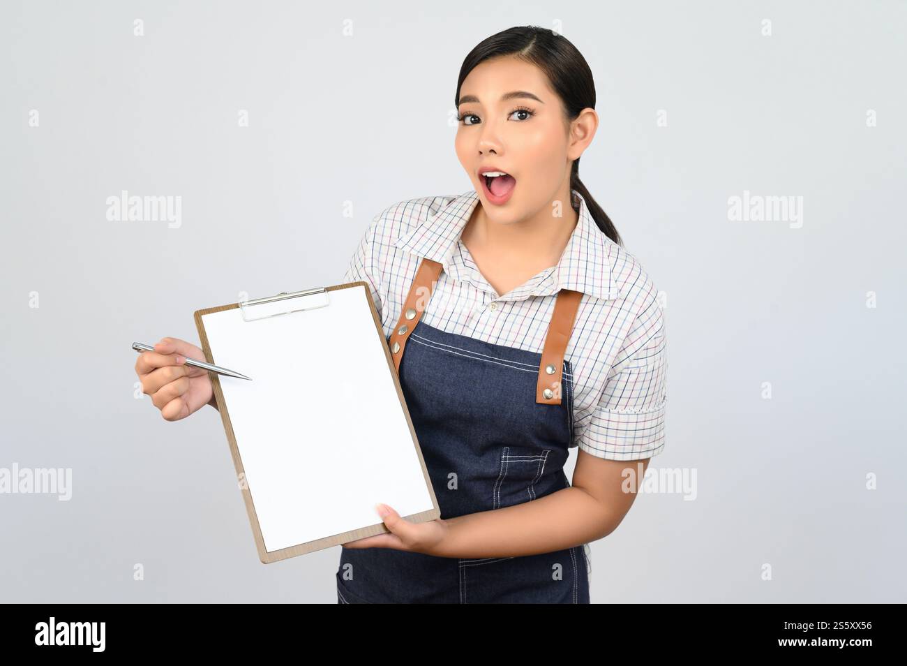 Portrait de jeune femme asiatique en uniforme de serveuse tenant maquette de presse-papiers avec stylo, espace de copie pour insérer du texte pour la publicité isolé sur blanc Banque D'Images